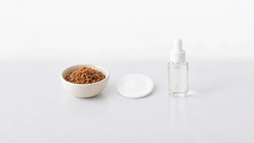 Bowl of scrub granules and a bottle of liquid exfoliant with a cotton pad