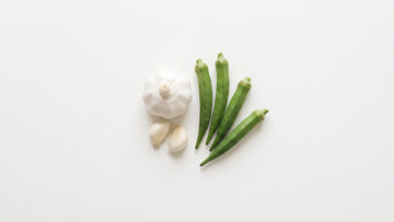 A garlic bulb, peeled cloves and fresh okra pods on a white table
